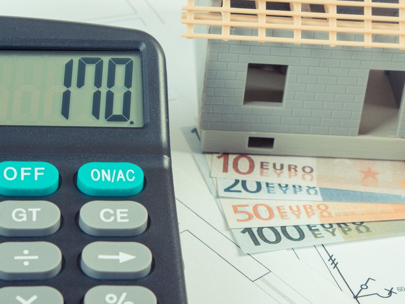 Calculadora junto a unos billetes de euro y una maqueta de casa sobre unos planos