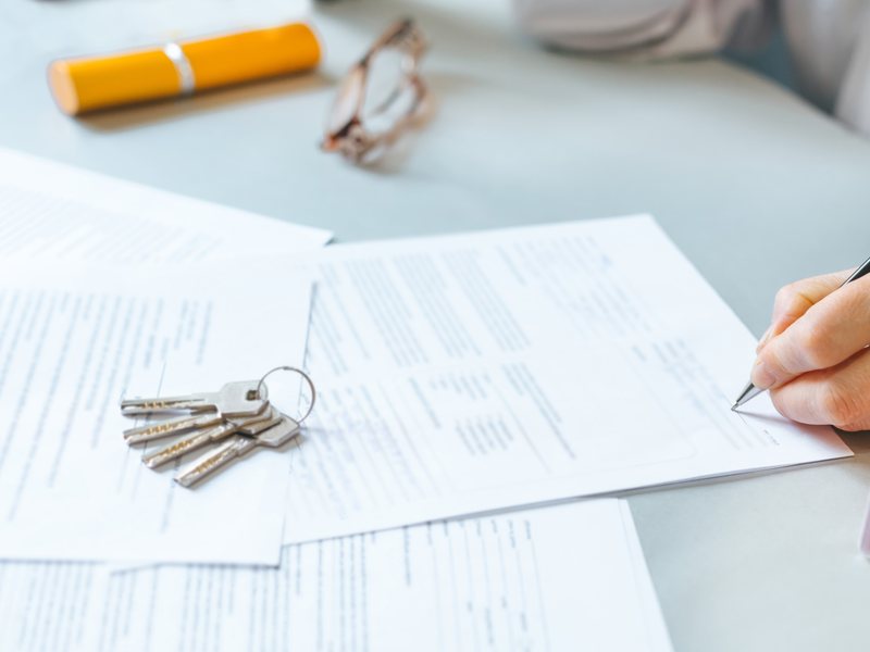Una mano firma un contrato sobre una mesa, con un juego de llaves encima de los papeles