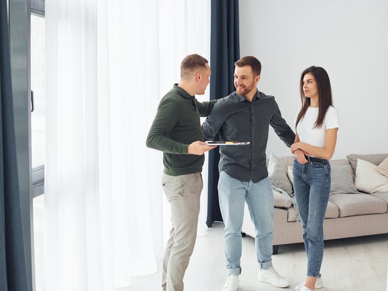 Pareja joven visitando con el propietario un piso luminoso que podría comprar