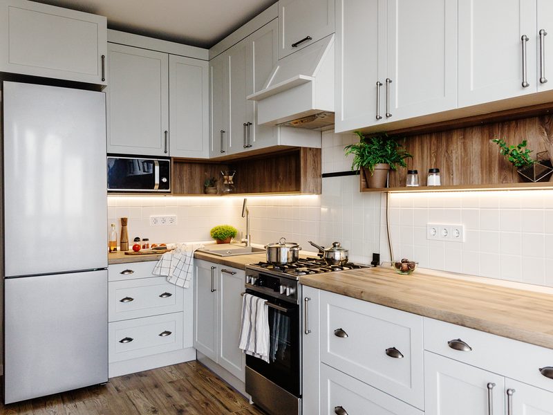 Cocina luminosa y recogida, con muebles blancos, nevera, horno de acero y encimera de madera