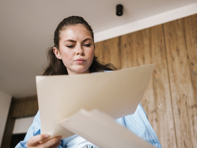Mujer en su casa que revisa con gesto serio unas hojas de papel
