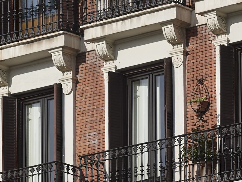 Fachada de un edificio de viviendas de ladrillo rojo con balcones de hierro forjado y contraventanas de madera