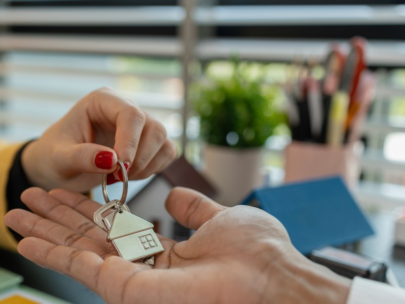 Entrega de unas llaves con un llavero en forma de casa en la palma de una mano