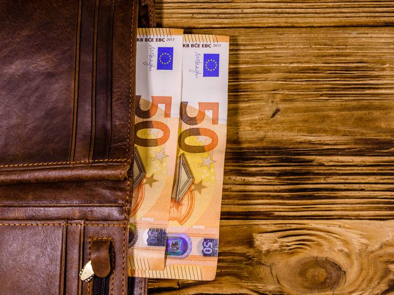 Dos billetes de 50 euros asoman de una cartera de piel marrón sobre una mesa de madera