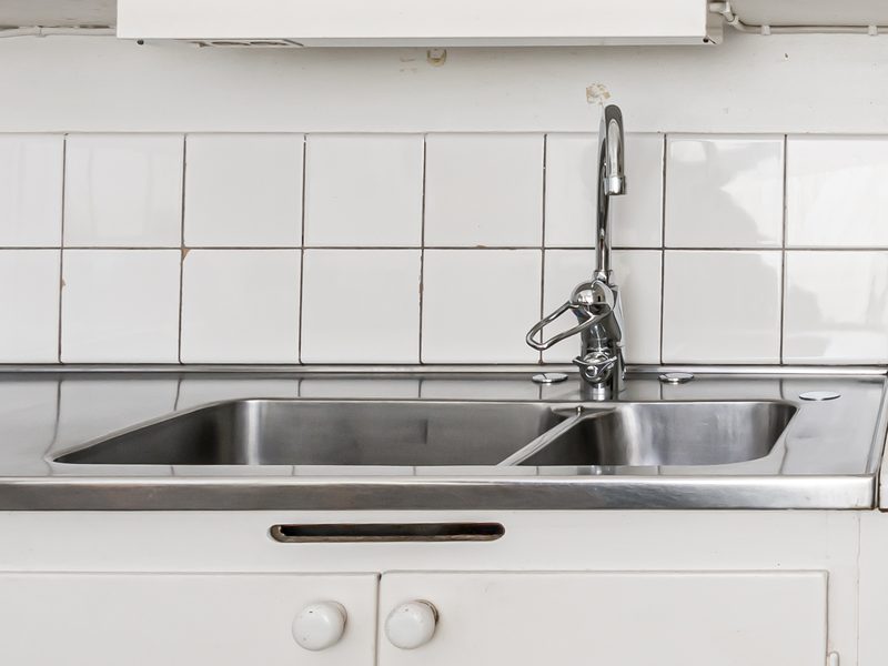 El grifo y el fregadero de acero de una cocina sencilla, con azulejos blancos