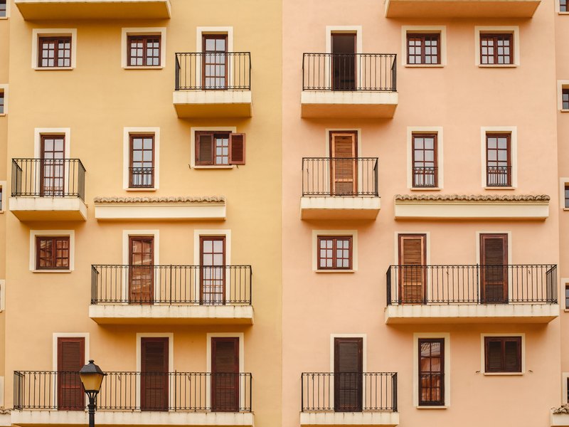 Fachada de un bloque de viviendas de estuco ocre y salmón, con balcones de forja y contraventanas de madera