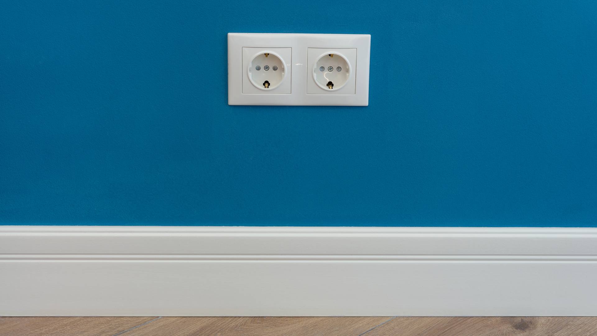 Un enchufe doble de pared en una pared azul, sobre el rodapié blanco